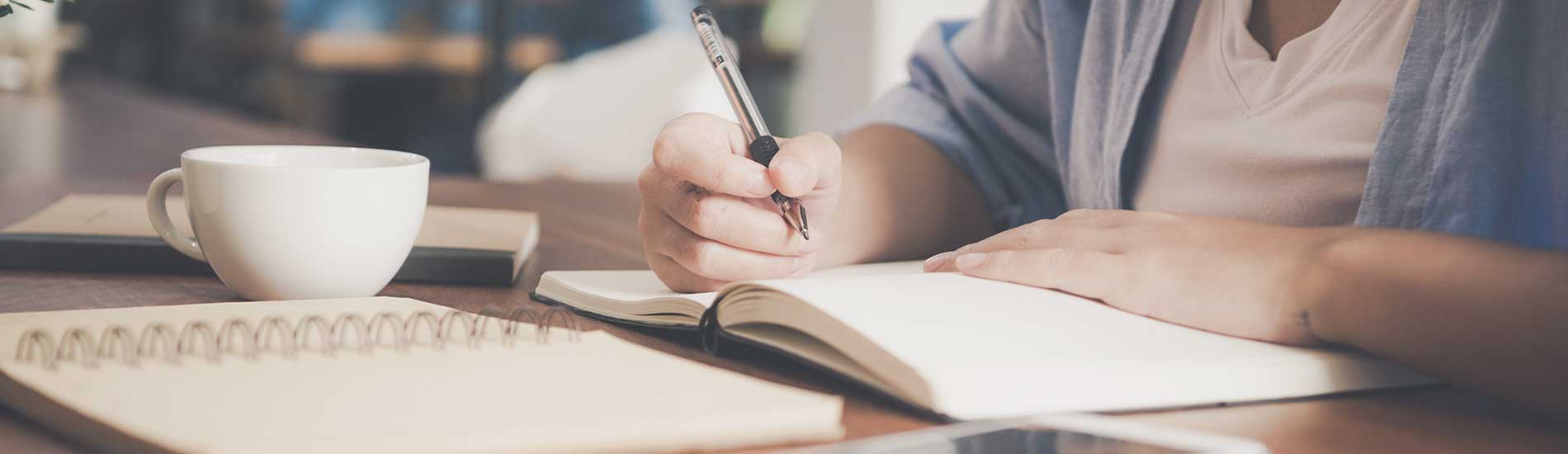 person studying and making notes with coffee cup on table