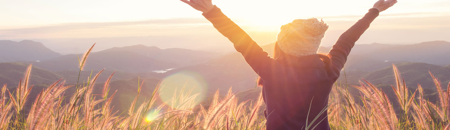 Woman with outstretched hands to Sun coming over mountain range